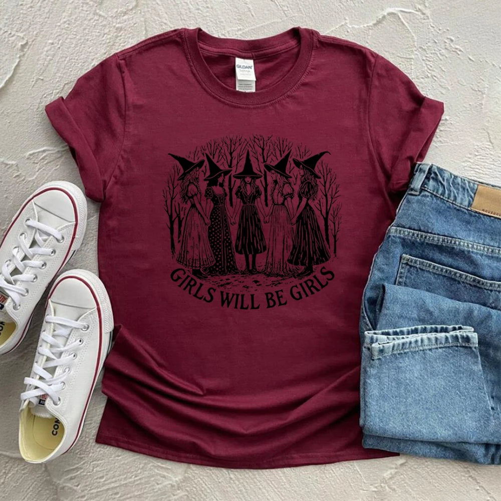 Maroon t-shirt with witch graphic and 'Girls Will Be Girls' text, paired with jeans and sneakers on a light background.