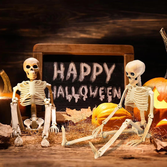 Two skeletons in front of a chalkboard with 'Happy Halloween' on a wooden table with pumpkins.