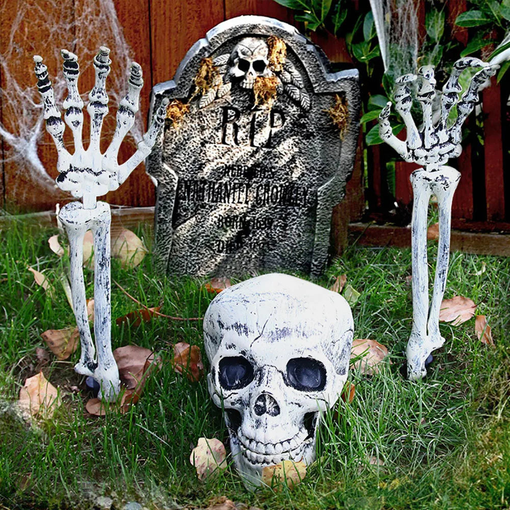 Halloween decorations including a tombstone, skeletons, and skulls on grass.
