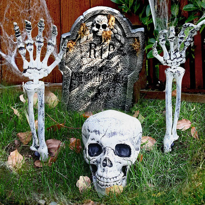 Halloween decorations including a tombstone, skeletons, and skulls on grass.