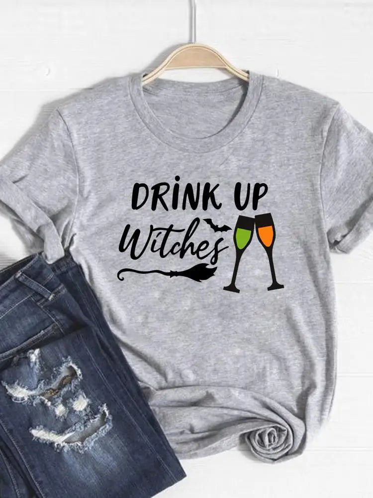 Gray t-shirt with 'Drink Up Witches' text and wine glass graphics on a hanger with jeans below.